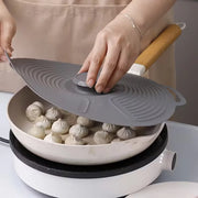 Person using a silicone lid to cover dumplings in a frying pan on a stove.