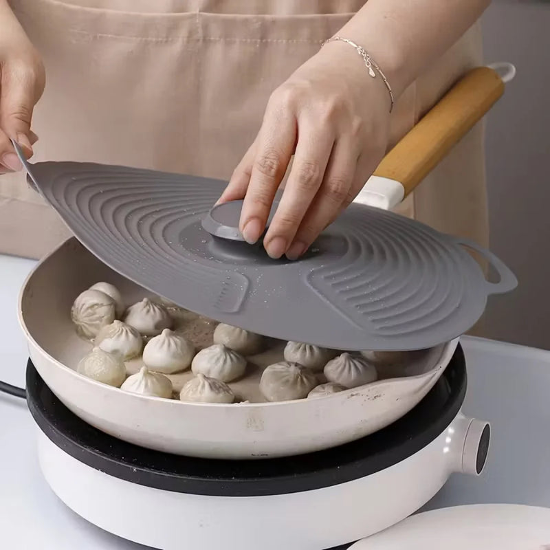 Person using a silicone lid to cover dumplings in a frying pan on a stove.