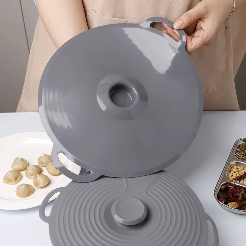 Gray silicone lid held by a person on a white surface with food items in the background