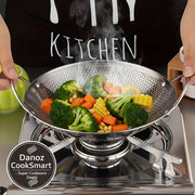 Metallic wok on a stove with a person wearing a black apron with 'KITCHEN' text.
