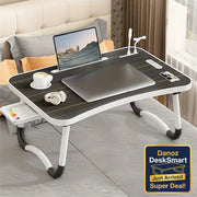 Foldable laptop desk with a laptop, coffee cup, and remote control on a bed.