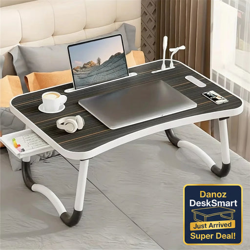 Foldable laptop desk with a laptop, coffee cup, and remote control on a bed.
