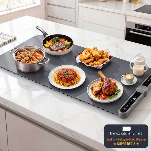A smart electric skillet set on a white marble kitchen countertop, surrounded by various cooked foods like pasta, shrimp, chicken, and a steak. The dark gray smart pan features a digital control panel on the side.