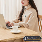 Person wearing a beige heated coat using a laptop with a cup of coffee on a wooden table.