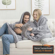 Two people sitting on a couch with a gray blanket wrapped around them, holding a cat.