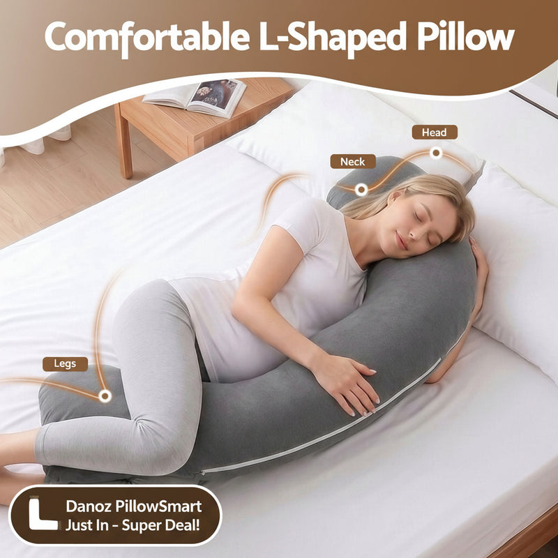 A woman lies on a bed using a large U-shaped body pillow with labeled callouts for head, neck, and legs. The pillow is dark gray, and the scene includes a bed, pillows, and a decorative top banner reading 'Comfortable L-Shaped Pillow.