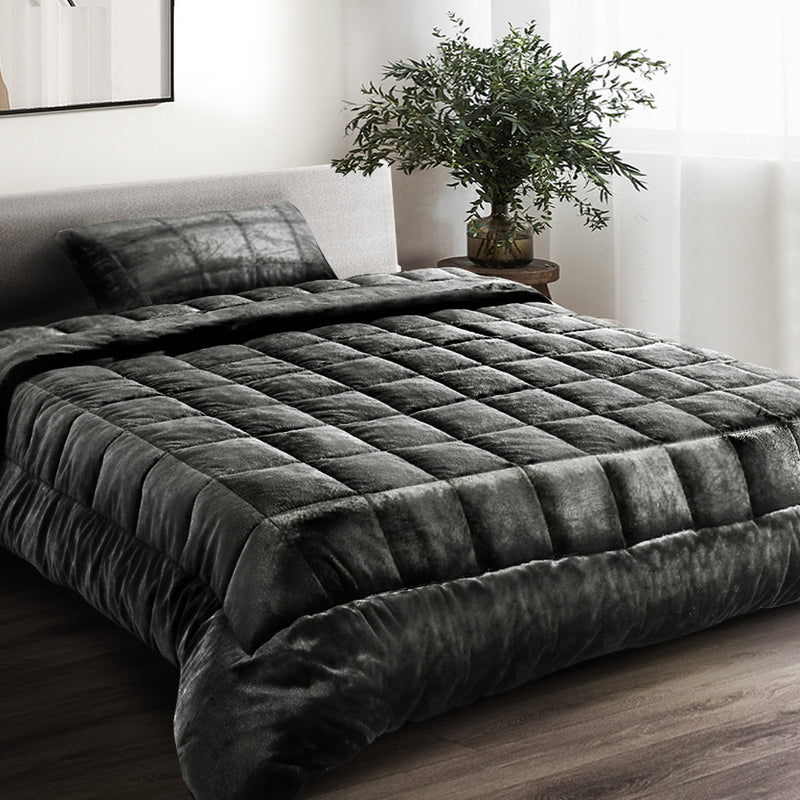 A charcoal-colored faux mink quilt with a double-sided design, displayed on a bed in a room with a neutral decor.