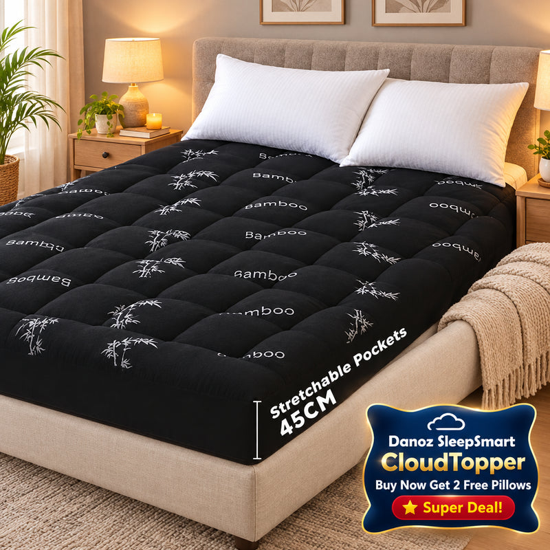 A black tufted mattress topper or mattress shown on a bed in a bedroom setting, with white pillows, a bedside lamp, and a green wall panel visible. The topper has a subtle white bamboo pattern and text reading 'Stretchable Pockets 45CM'.