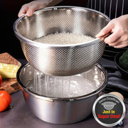Stainless steel colander with perforated design being used to drain rice, surrounded by kitchen items.