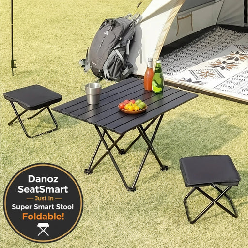 Camping setup with a black folding table, stools, and a backpack near a tent.