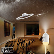 Room with a ceiling projector displaying a starry night sky and Saturn, with a small lamp on a surface.