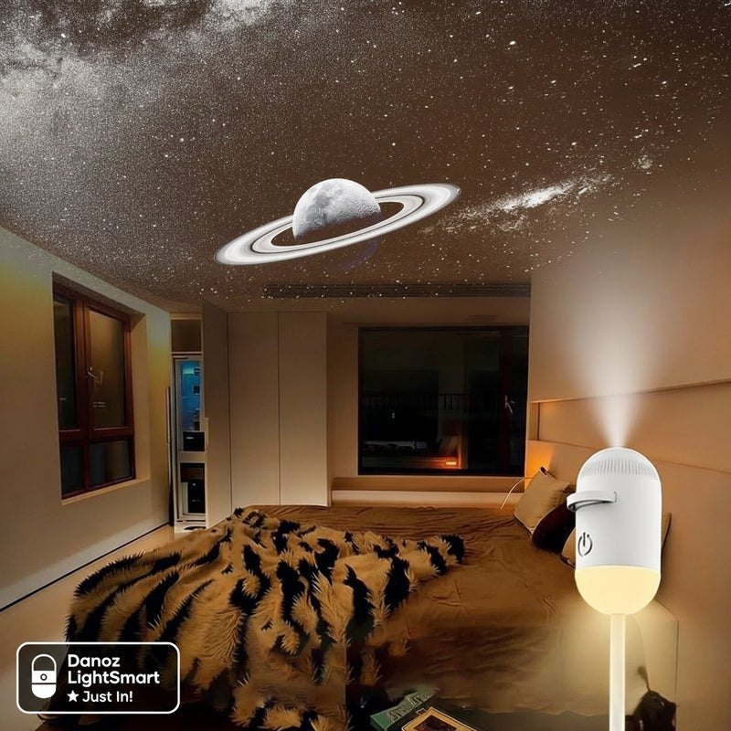 Room with a ceiling projector displaying a starry night sky and Saturn, with a small lamp on a surface.