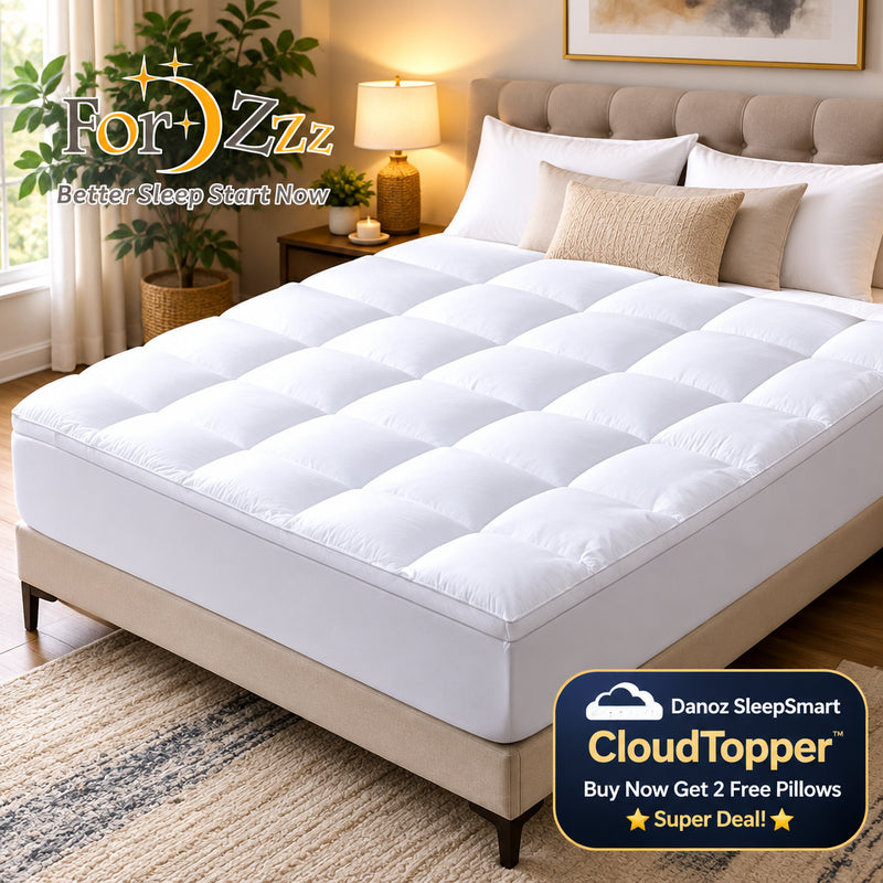A white tufted mattress protector or mattress pad shown on a bed in a styled bedroom setting, with white pillows, a dark upholstered headboard, bedside lamp, plant, and patterned rug visible.