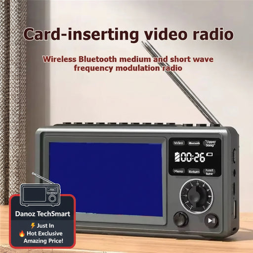 A gray card-inserting video radio with an extended antenna, shown on a wooden surface with a curtain in the background. The radio has a blue display screen, a digital display showing '200.