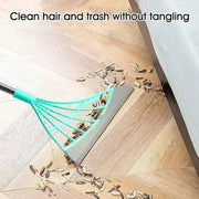 Teal leaf rake cleaning hair and trash from a wooden floor.