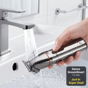 A close-up of a hand holding a metallic electric trimmer under running water in a sink.