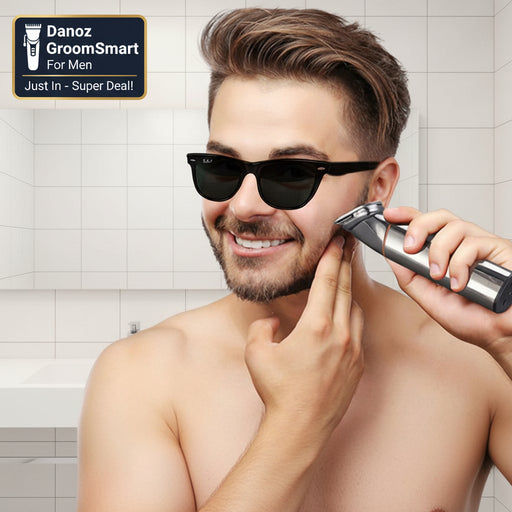 A man with sunglasses shaving his face with an electric trimmer, shown against a plain gray studio background.