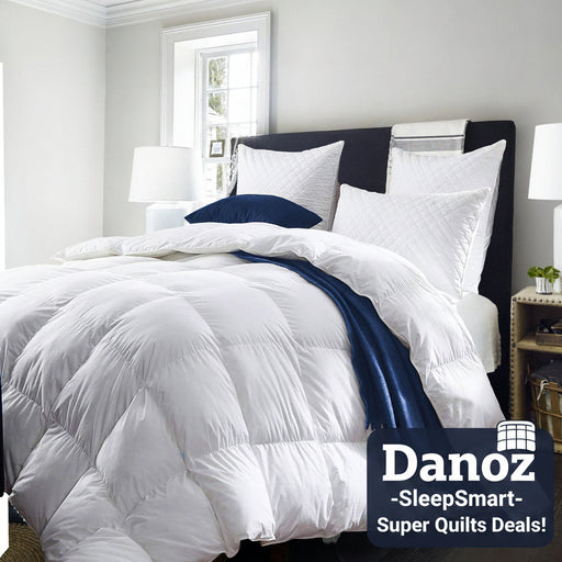 A double-sized white quilt displayed on a bed with a dark headboard, accompanied by pillows and a blue throw.