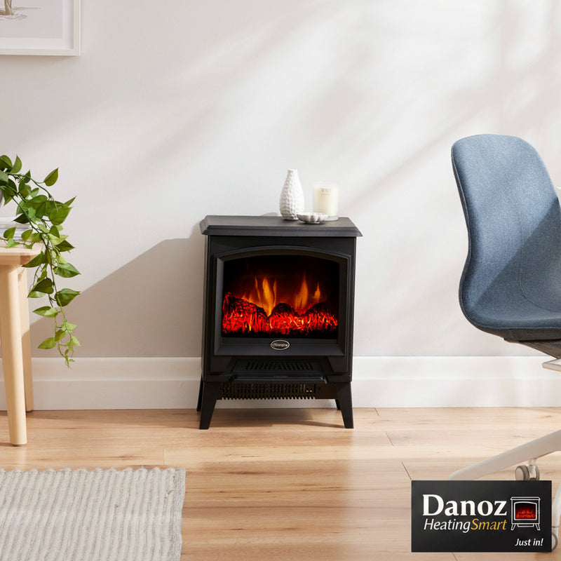 Small electric stove with fiery display in a room with a chair and plant.