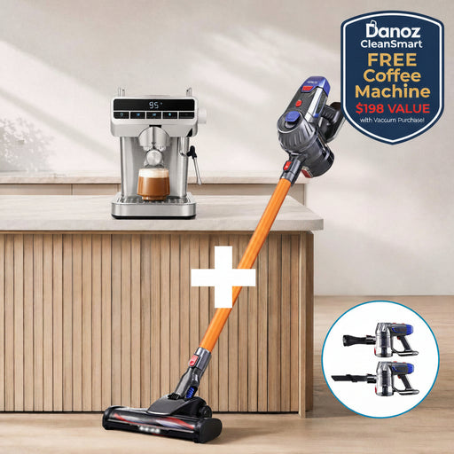 A cordless stick vacuum cleaner with an orange handle and dark blue/black body is shown on a wooden floor beside a countertop with a coffee machine. A circular inset at the bottom right shows two alternate heads for the vacuum.