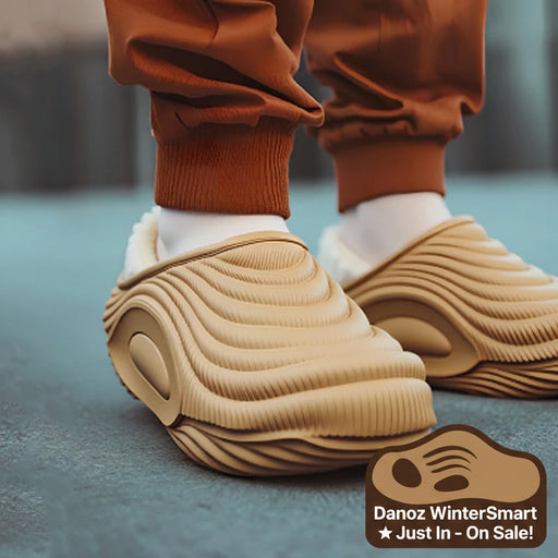 Beige slippers with textured sole worn by a person in brown pants and white socks.