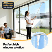 Woman cleaning a high window with a squeegee, with a man and child watching indoors.