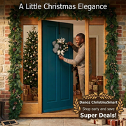 Man straightening a small champagne Christmas wreath on a teal door