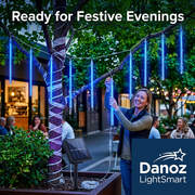 Woman decorating a tree with blue meteor lights for a garden celebration