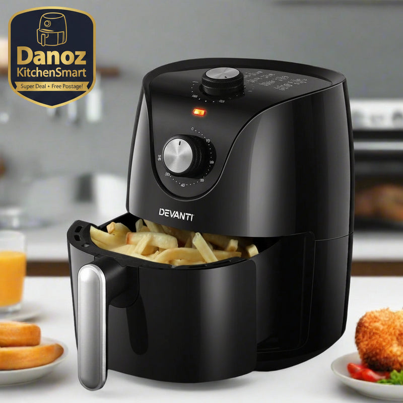 A black Devanti air fryer with french fries inside, placed on a kitchen countertop with a cool touch handle and non-slip feet. The surrounding area includes a glass of orange juice and some fruits.