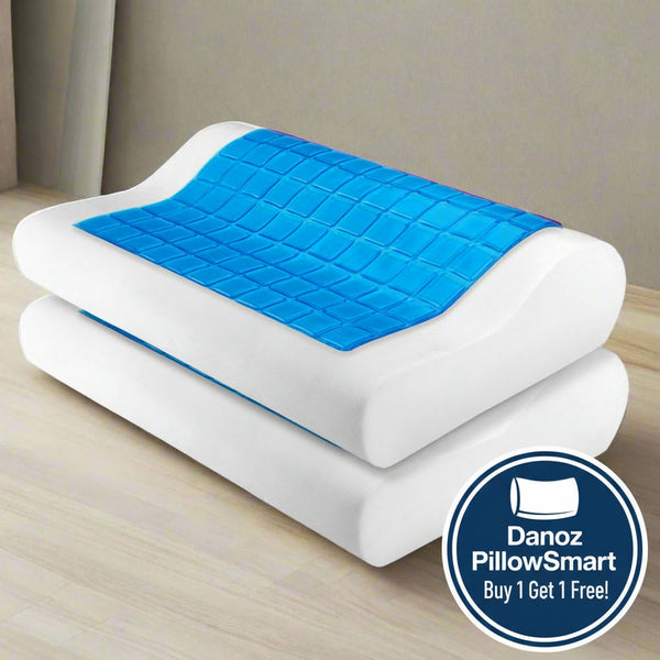 A white memory foam pillow with a blue cool gel layer on top, presented on a wooden surface with curtains in the background.