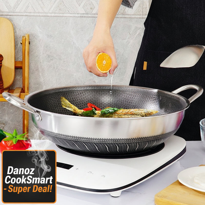 A person is stir-frying vegetables in a silver-colored double-sided honeycomb non-stick wok with a stainless steel handle, on a white cooking surface.